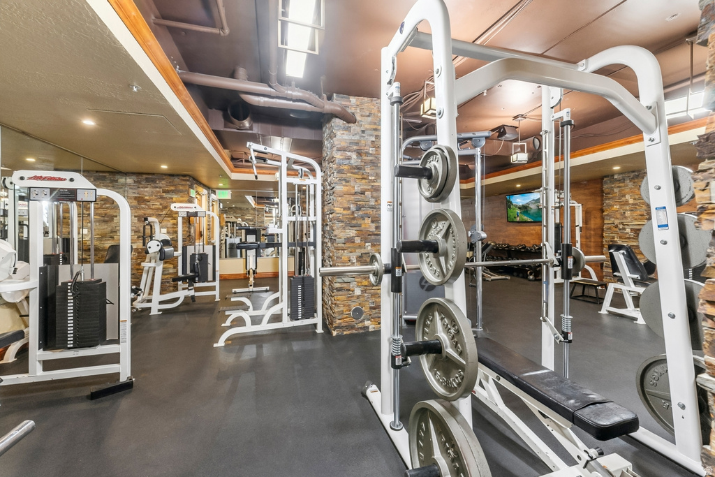 Dedicated fitness center featuring rubberized flooring, exposed industrial ceiling, stacked stone wall accents, and multiple weight machines