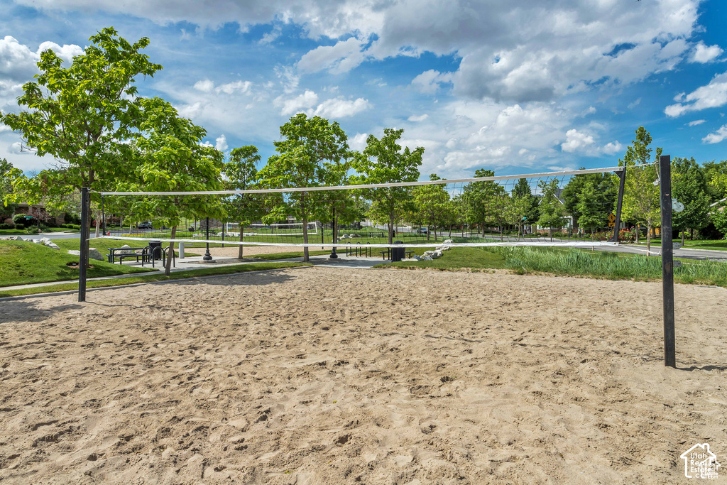 Sand volleyball court featuring a net and boundary lines, surrounded by green landscaping and mature trees