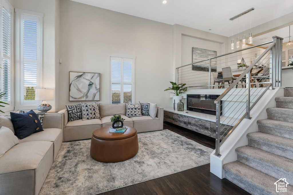 Soaring ceilings define this living space featuring tall windows with louvered shutters, dark wood-finish flooring, and a built-in fireplace with media console