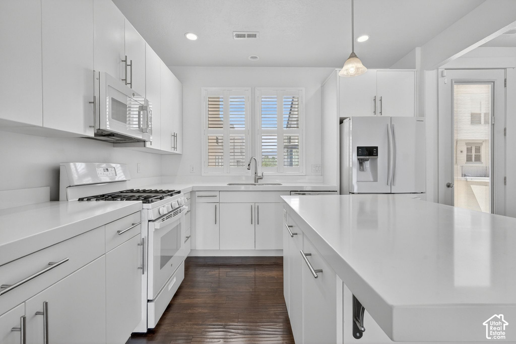 Modern white kitchen featuring a gas range, over-the-range microwave, double-door refrigerator, and a kitchen island with a white countertop