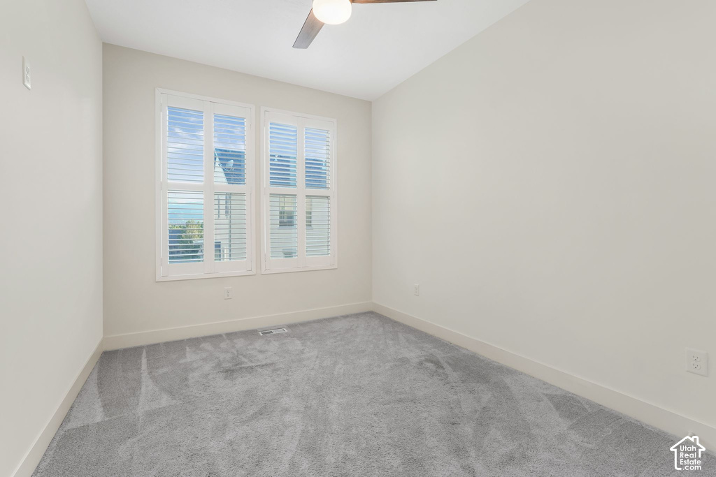 Neutral-toned room featuring a ceiling fan, dual windows with white plantation shutters, and gray patterned carpet