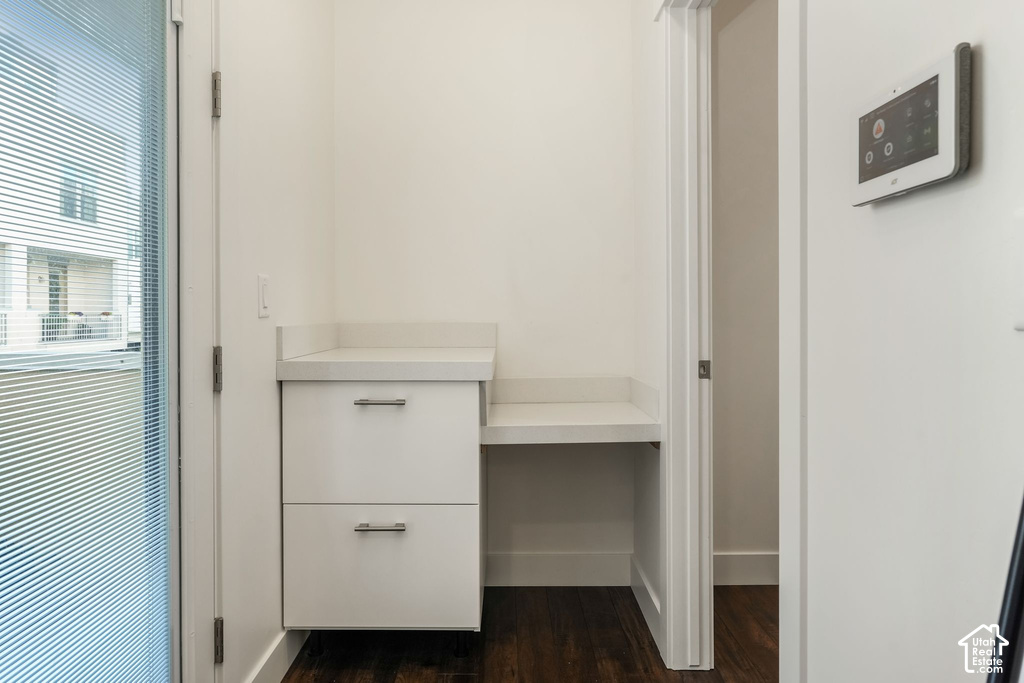 Built-in white cabinetry with a light countertop, integrated desk space, and dark wood-finish flooring