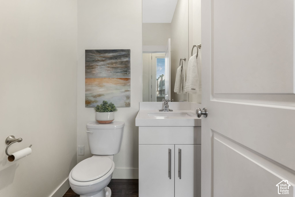 Powder room featuring a white single-sink vanity with storage, a white toilet, and wood-finish flooring