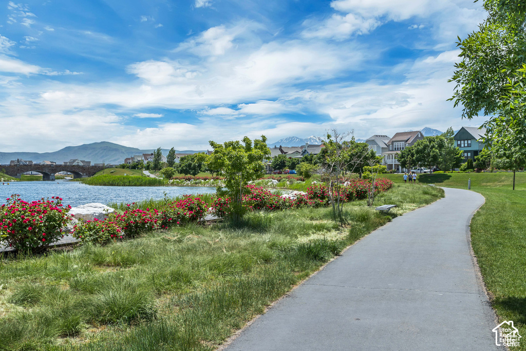 Paved pathway bordering a body of water with lush landscaping and distant mountain peaks
