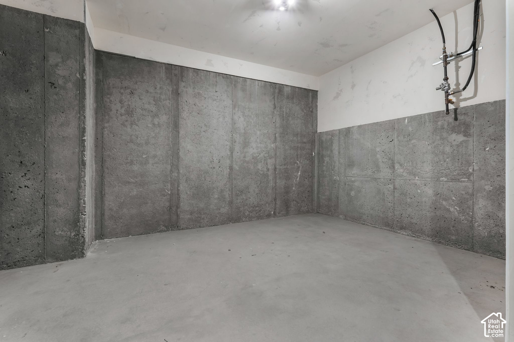 Concrete floor and walls, with partial drywall ceiling and upper wall sections, featuring exposed plumbing