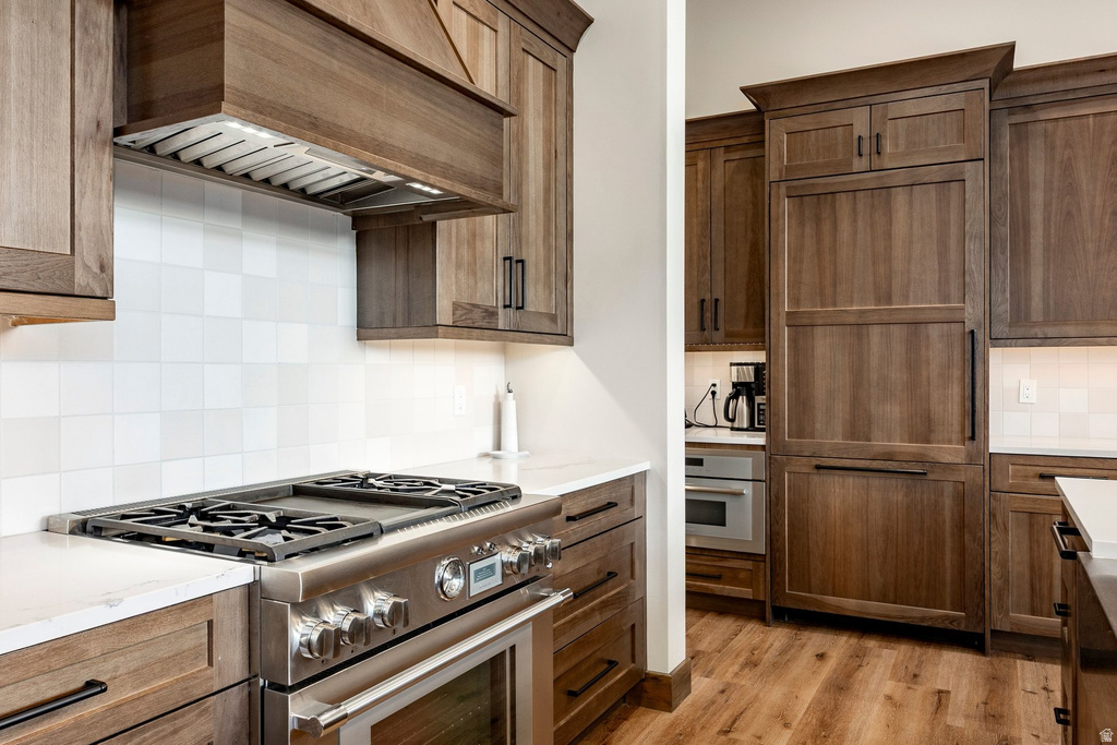 Gourmet kitchen featuring custom wood-finish cabinetry, stainless steel range with griddle, panel-ready refrigerator, white square tile backsplash, and light countertops