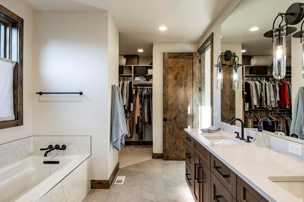 Bathroom featuring a double vanity with stone countertops, a built-in tub with matte black fixtures, an expansive walk-in closet, and wood-finish flooring