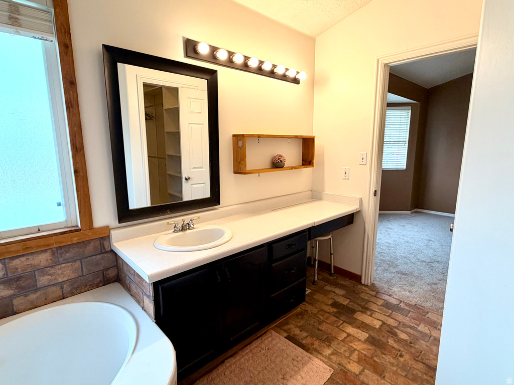 Spacious bathroom featuring a built-in soaking tub, an extended vanity with an integrated sink, a large framed mirror, and a brick-patterned floor