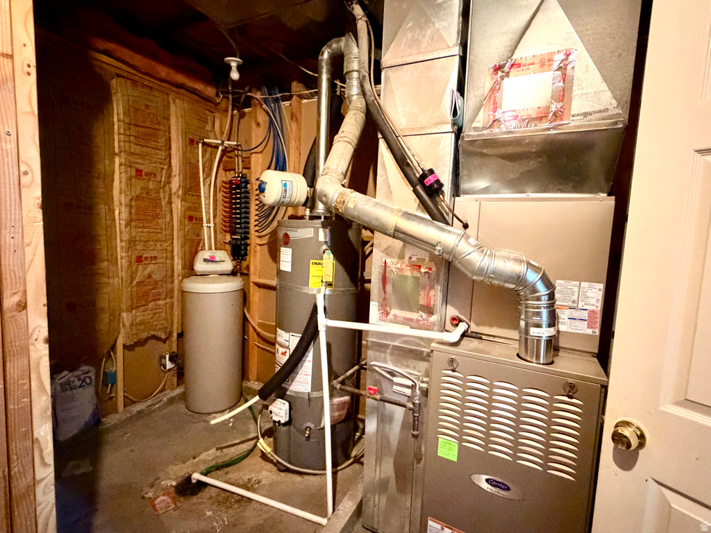 Utility room featuring a water heater, furnace, and exposed insulation within unfinished wood framing