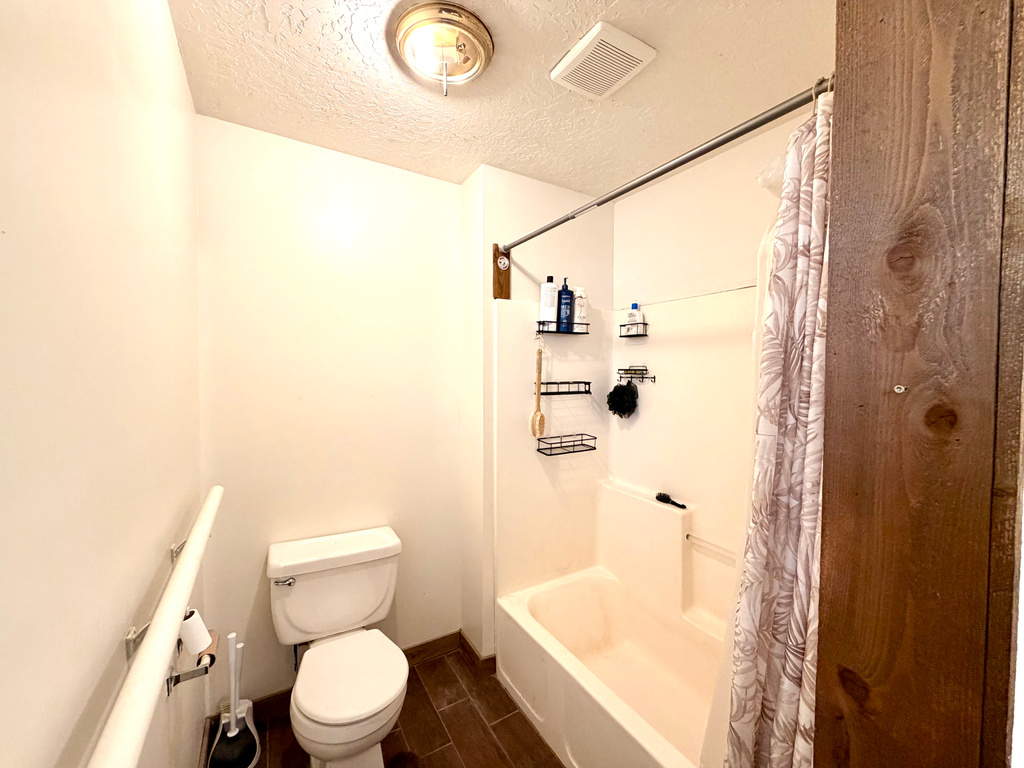 Full bathroom featuring a white tub/shower combination, white toilet, and wood-finish flooring