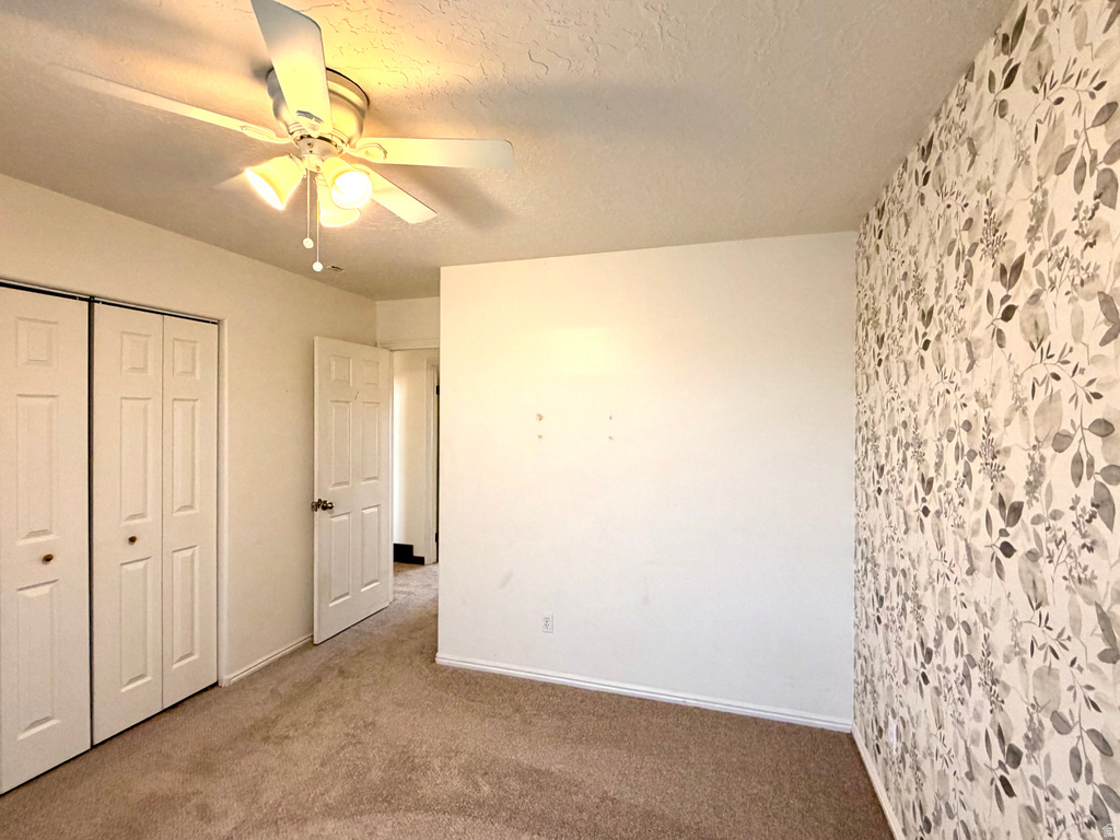 Carpeted room featuring a ceiling fan with integrated lighting, decorative floral wallpaper accent wall, white bi-fold closet doors, and white interior doors