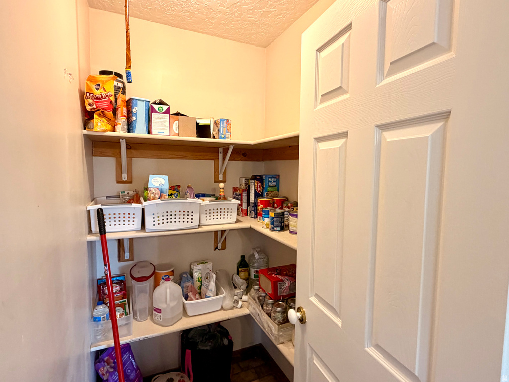 Pantry featuring multiple levels of wood shelving, white paneled door, and textured ceiling
