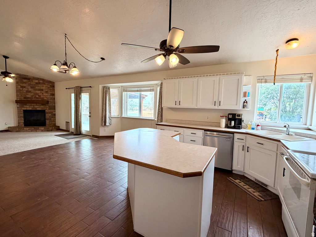 Open-concept living space featuring wood-finish flooring, a brick fireplace with a wood mantle, and a kitchen island with a light-colored countertop