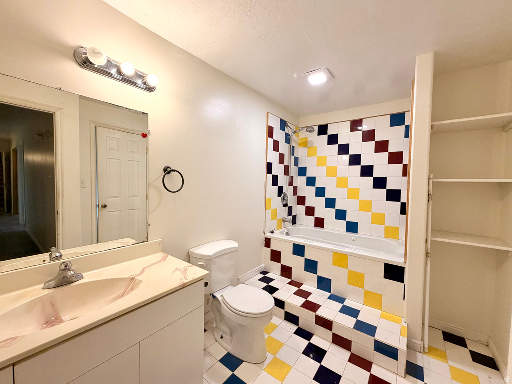 Bathroom featuring a full-size bathtub with a tiled surround, a vanity with a cultured marble countertop and integrated sink, a toilet, and built-in shelving