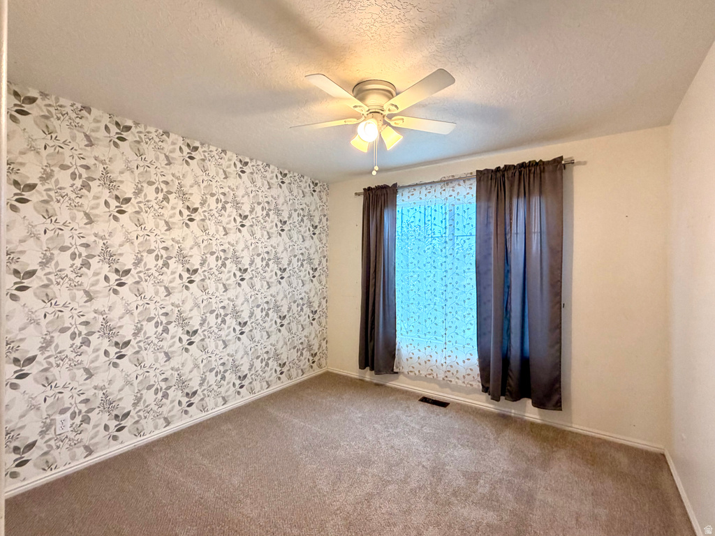 Carpeted room featuring a decorative accent wall with botanical pattern, white baseboards, and a ceiling fan with integrated lighting