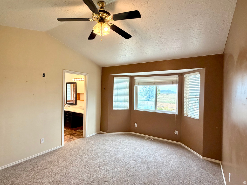 Spacious room featuring vaulted ceilings, a bay window with blinds, and neutral carpeting