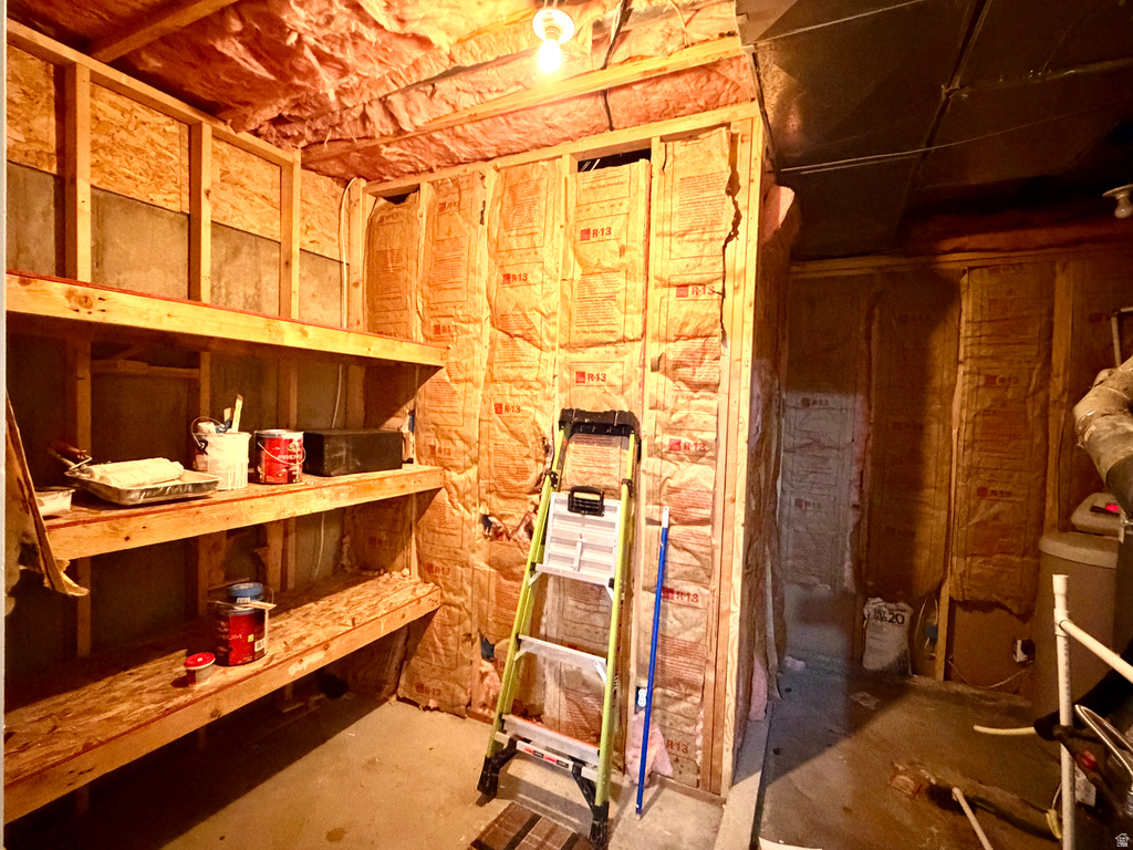 Unfinished basement area featuring exposed wood framing, installed insulation, and built-in wooden shelving for storage