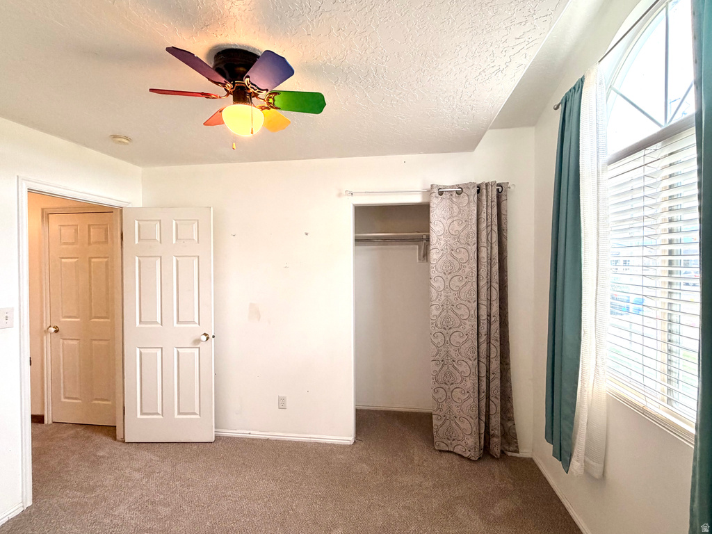 Carpeted interior space featuring a multi-pane arched window with blinds, a built-in closet with hanging rod, and a ceiling fan with integrated lighting