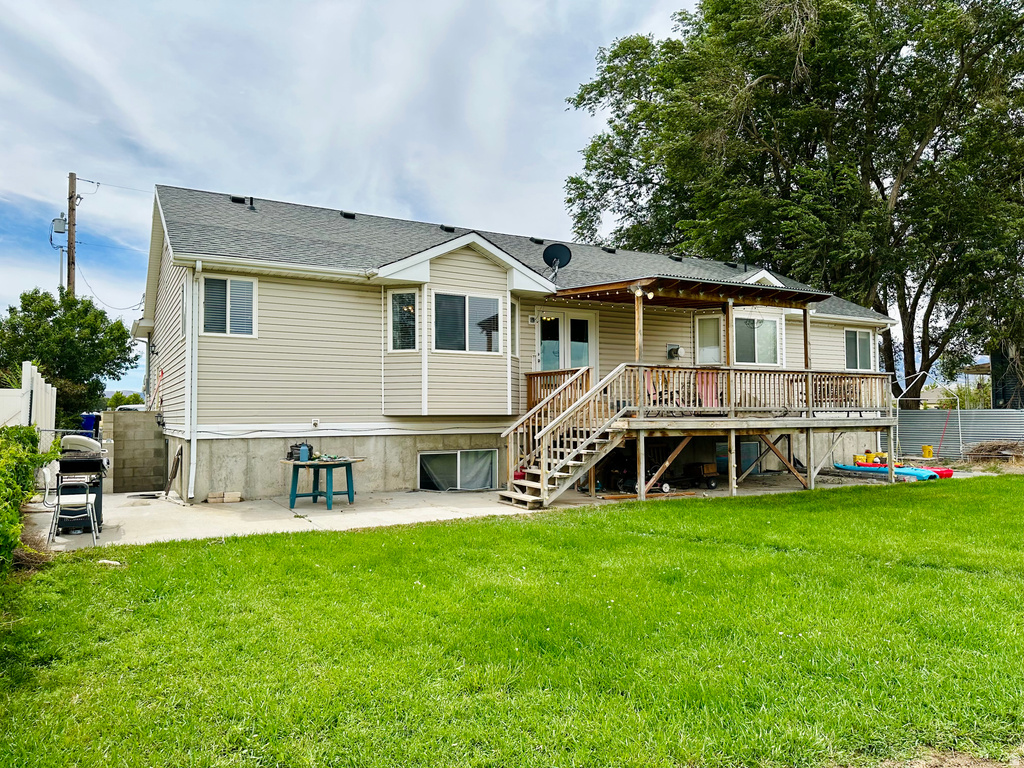 Rear exterior featuring a spacious wooden deck with a covered portion, direct access to the yard, and a ground-level concrete patio