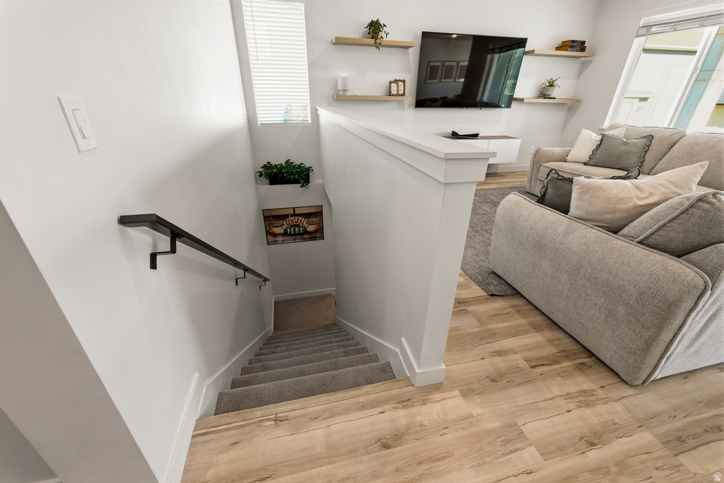Carpeted staircase with a matte black handrail, wood-finish flooring, and a white balustrade