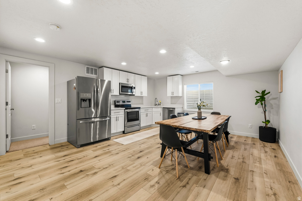 Open-concept living area featuring wood-finish flooring, a full kitchen with stainless steel appliances, white cabinetry, and recessed lighting