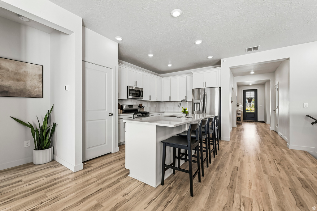 Kitchen featuring a central island with countertop seating, white cabinetry, stainless steel appliances, and wood-finish flooring