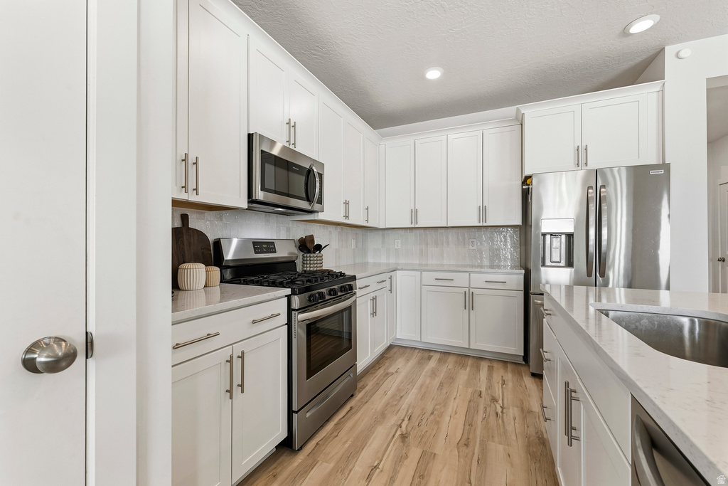 Contemporary kitchen featuring white cabinetry, light-colored countertops, stainless steel appliances, a subway tile backsplash, and wood-finish flooring