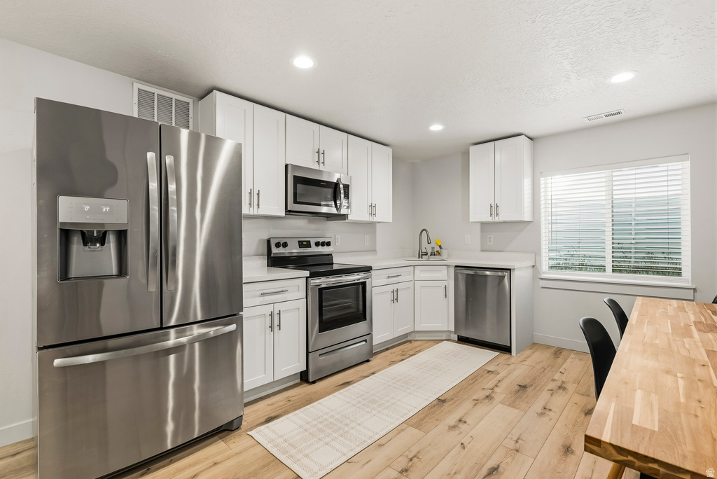 Kitchen featuring stainless steel appliances, white cabinetry, light-toned countertops, and wood-finish flooring