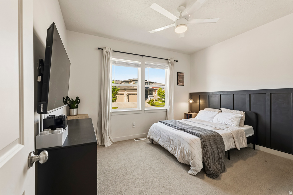 Carpeted bedroom featuring a large window, ceiling fan with integrated lighting, and a built-in paneled accent wall