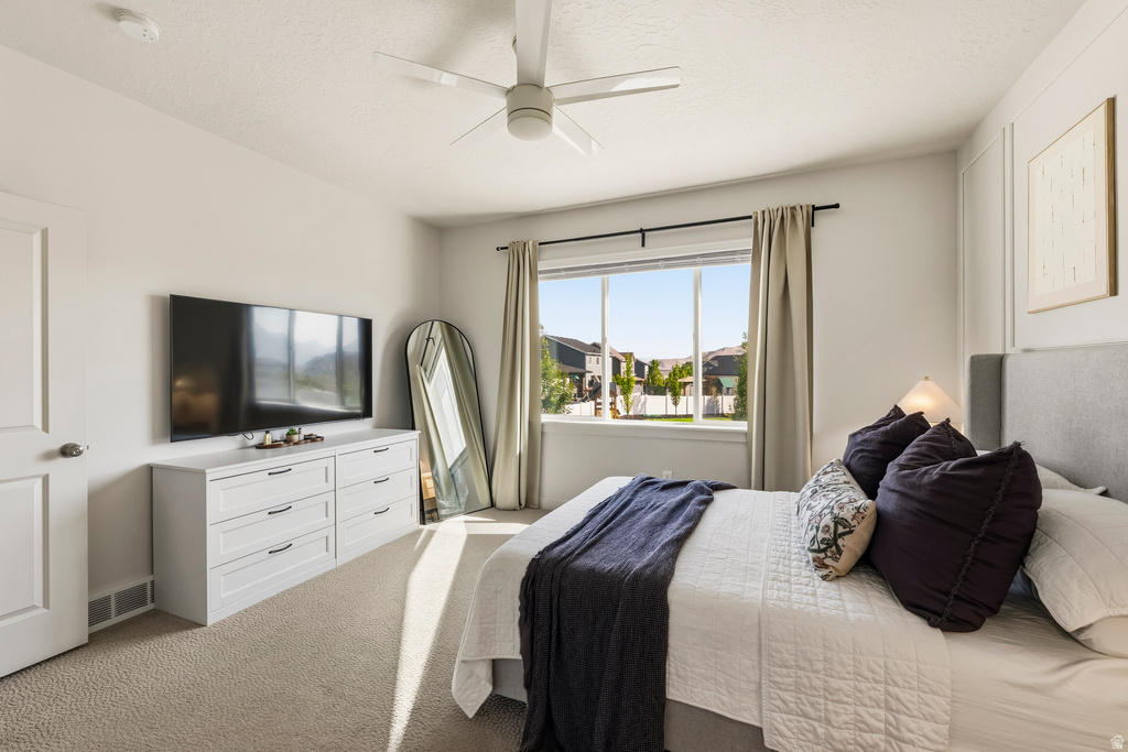 Carpeted bedroom featuring a ceiling fan, a large window with curtain rods, and a white six-drawer dresser