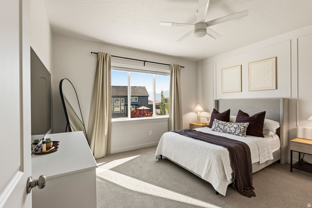 Carpeted bedroom featuring a large window, ceiling fan, and wall paneling