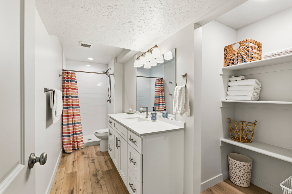 Bathroom featuring a white vanity with dual sinks, a shower with white subway tile surround, wood-finish flooring, and built-in shelving