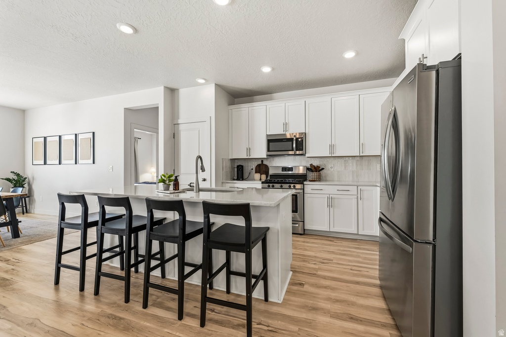 Modern kitchen featuring a central island with countertop seating, stainless steel appliances, white cabinetry, and wood-finish flooring