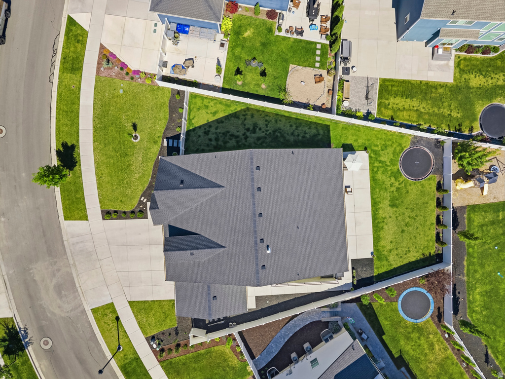 Aerial view highlighting a dark shingled roof, extensive concrete patio space, and manicured green lawns