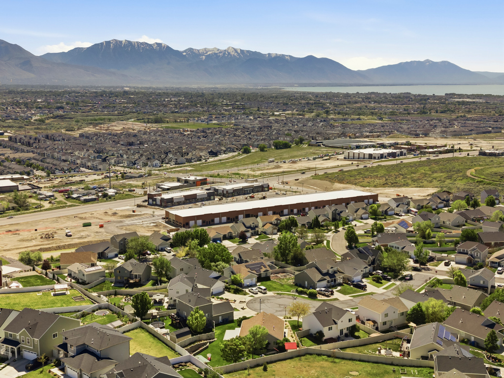 Expansive neighborhood aerial showcasing residential homes with a backdrop of snow-capped mountains and a large body of water