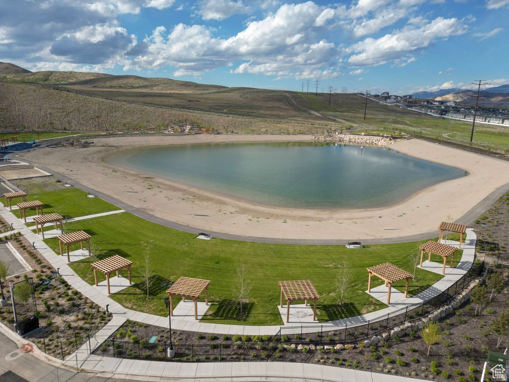 Lakefront property featuring a sandy beach, green lawn, paved walking paths, and several pergolas