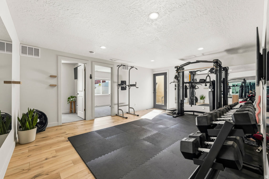 Dedicated fitness area featuring light wood-finish flooring, recessed lighting, and a full-length wall mirror