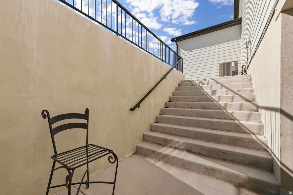 Concrete staircase with black metal handrail and railing, bordered by stucco walls and a white siding structure