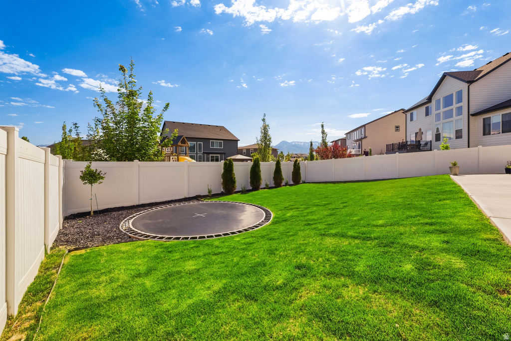 Expansive fenced backyard featuring a vibrant green lawn, mature trees, and a concrete patio area
