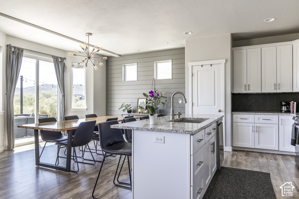 Open-concept kitchen and dining area featuring a central island with a sink, white cabinetry with silver hardware, granite countertops, and a black herringbone backsplash