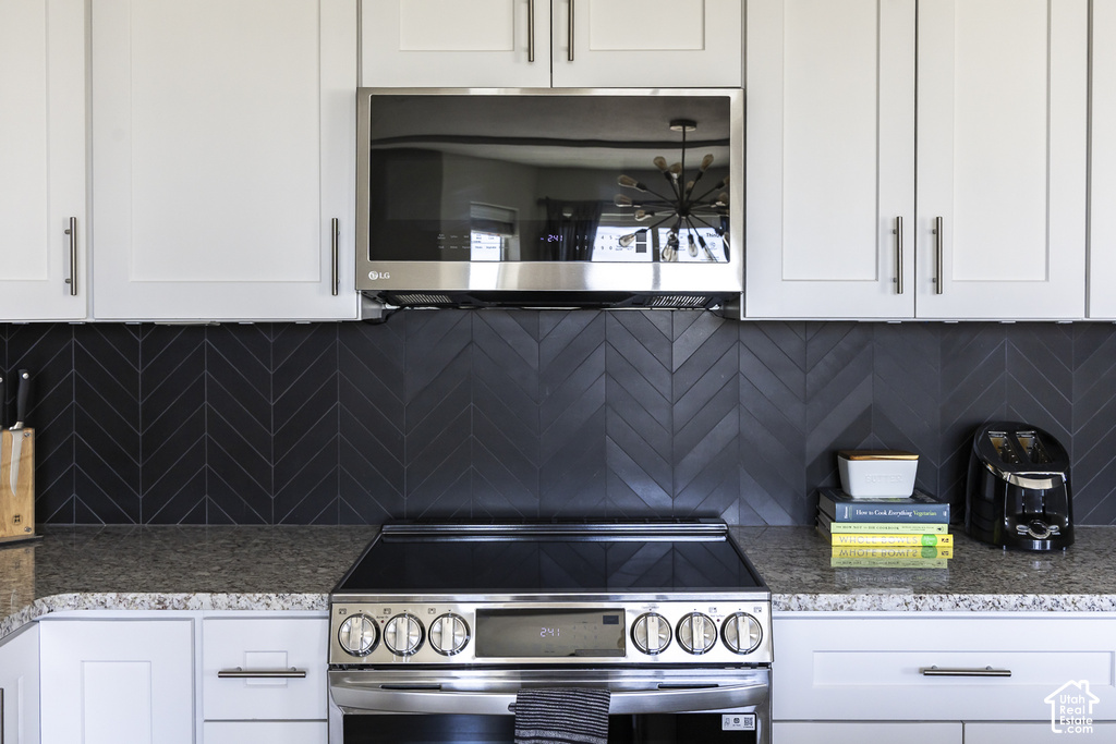 Kitchen featuring dark herringbone tile backsplash, stainless steel range, built-in microwave, white upper and lower cabinetry, and granite-style countertops