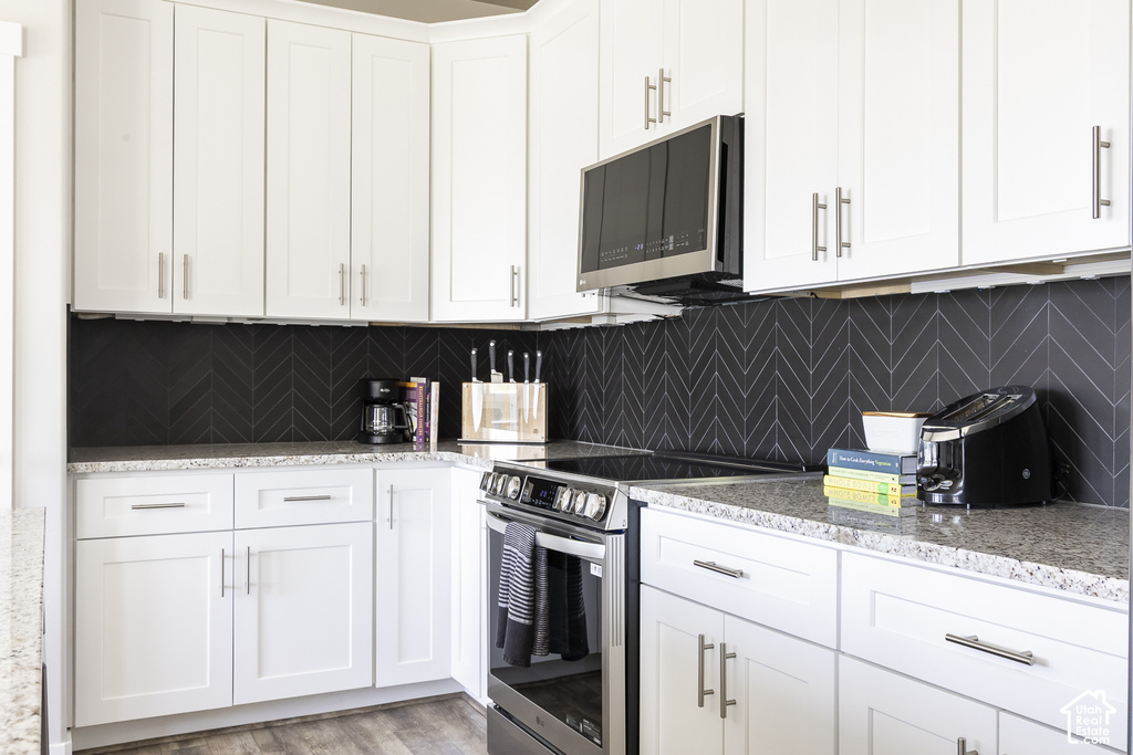Modern kitchen featuring white shaker cabinetry, stainless steel appliances, speckled stone countertops, a patterned dark backsplash, and wood-finish flooring