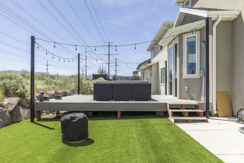 Elevated composite deck with string lighting, artificial turf, stucco exterior, and a rock retention wall