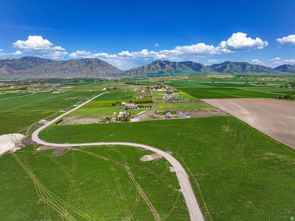 Expansive green fields surrounding a developing residential area with distant mountains under a clear sky