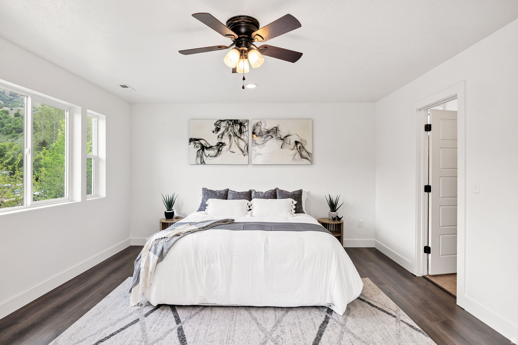 Spacious room featuring multiple windows, dark wood-finish flooring, a ceiling fan with integrated lighting, and a paneled door