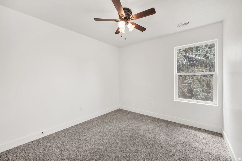 Room featuring textured grey carpet, white walls, a single window, and a ceiling fan with integrated lighting