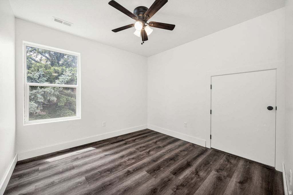 Room featuring wood-finish flooring, a white window, a white door with a black knob, a ceiling fan with light fixture, and white baseboards