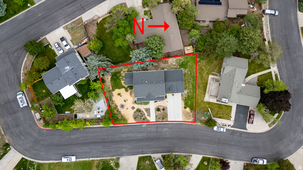 Aerial view of a residential property on a curved street, featuring a grey-roofed dwelling with a paved driveway