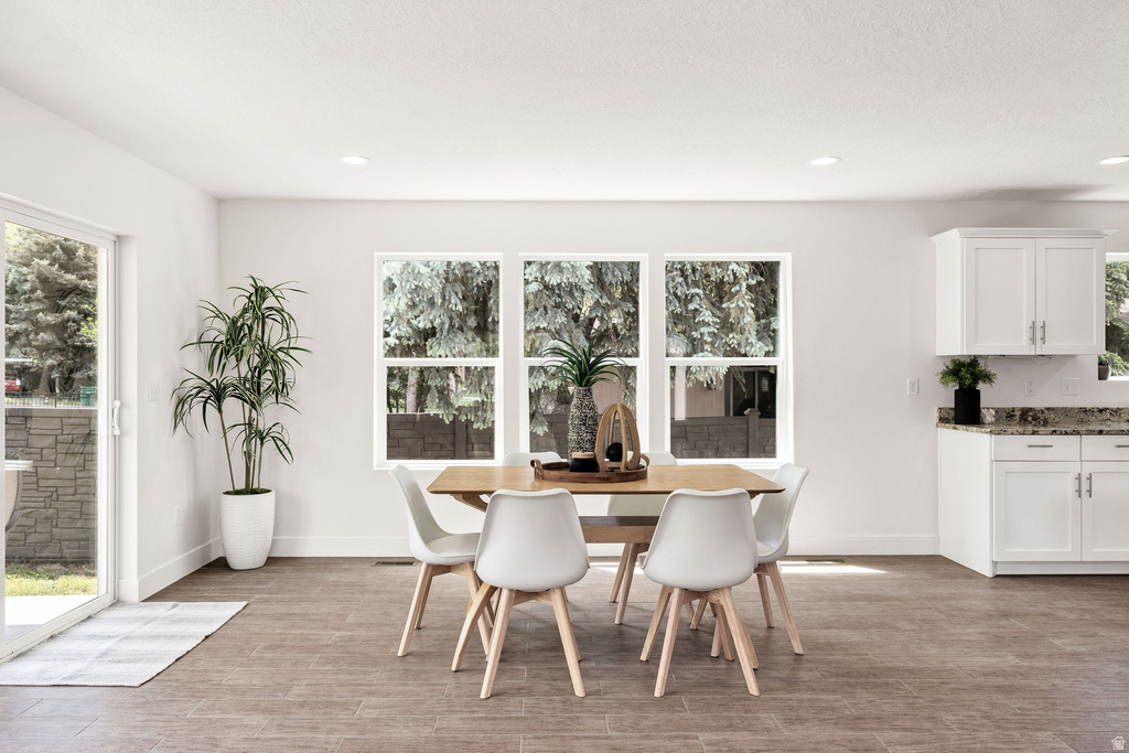Dining area featuring wood-finish flooring, three large windows, recessed lighting, and a sliding glass door