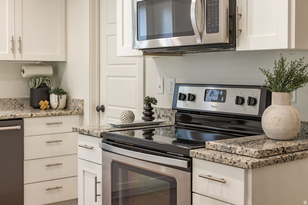 Modern kitchen featuring white cabinetry with brushed nickel hardware, granite countertops, stainless steel appliances, and a built-in microwave